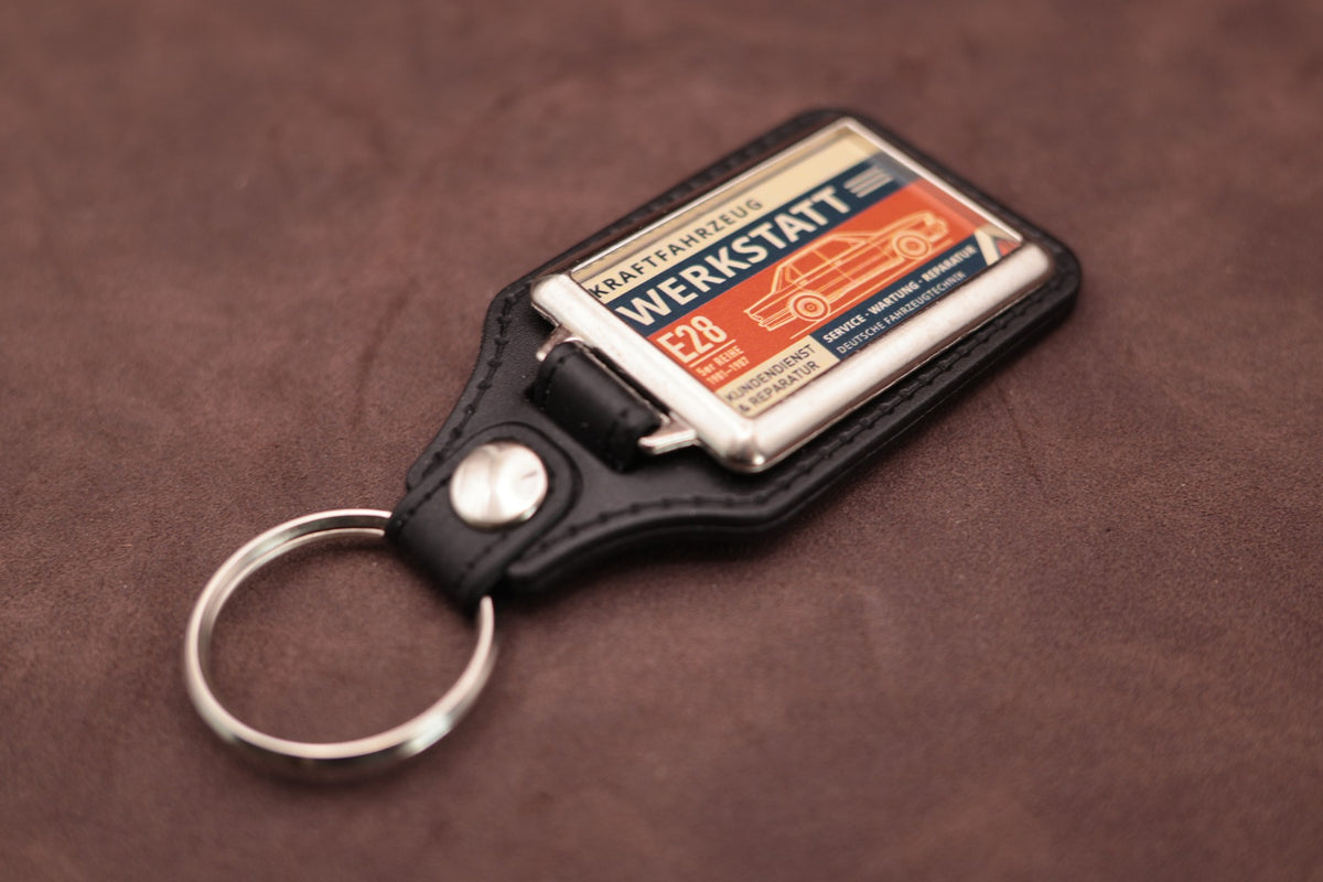 BMW E28 Werkstatt keyring angled with the split ring at lower left, showing the printed label and black leatherette fob
