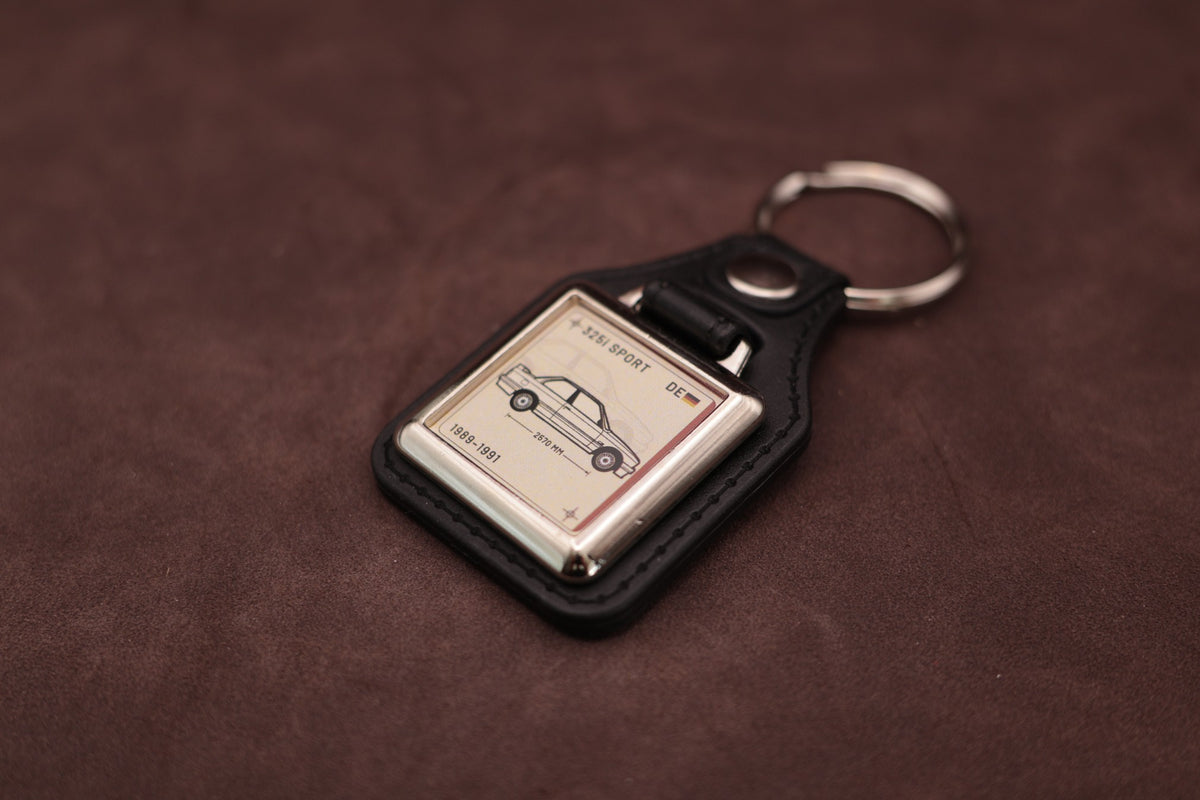 BMW E30 325i Register Series keyring angled with the split ring at upper right and ivory vehicle artwork visible