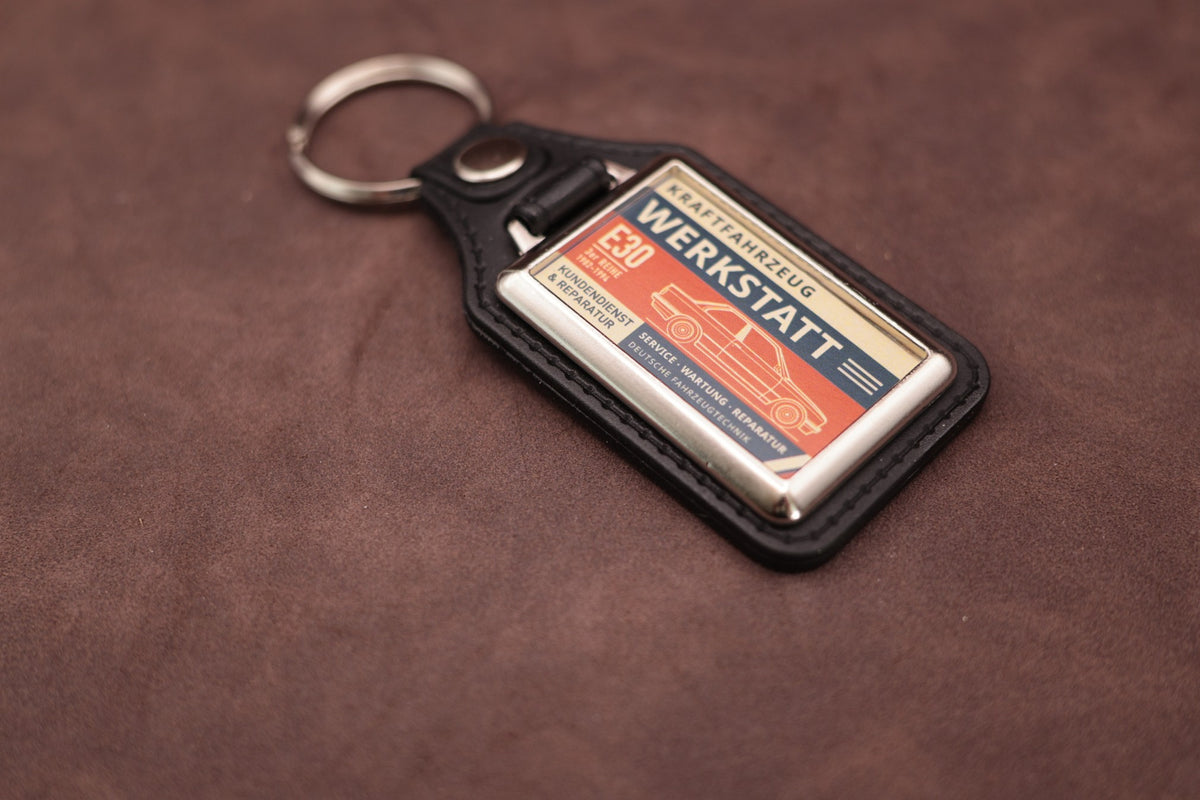 BMW E30 Werkstatt keyring angled with the split ring at lower left, showing the printed label and black leatherette fob