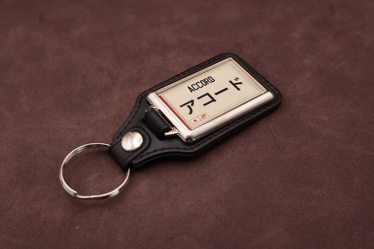 Honda Accord Katakana keyring angled with the split ring at lower left, showing the cream insert and black leatherette fob