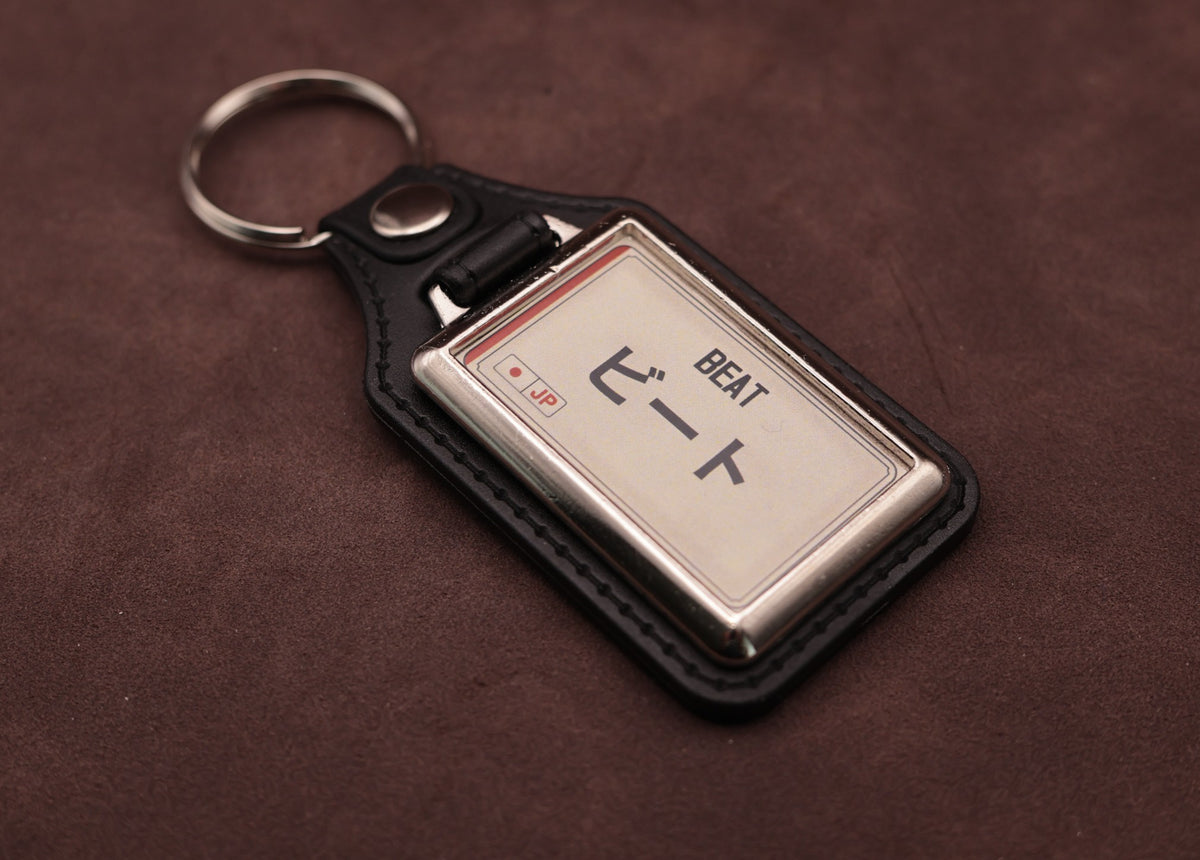 Honda Beat Katakana keyring angled with the split ring at upper left, showing the printed insert and chromed frame