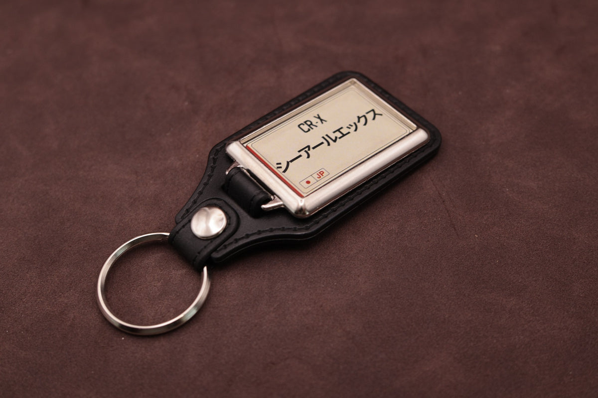 Honda CR-X Katakana keyring angled with the split ring at lower left, showing the cream insert and black leatherette fob