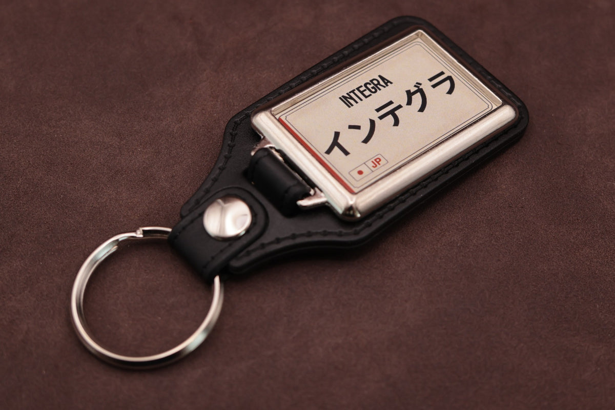 Honda Integra Katakana keyring angled with the split ring at lower left, showing the cream insert and black leatherette fob