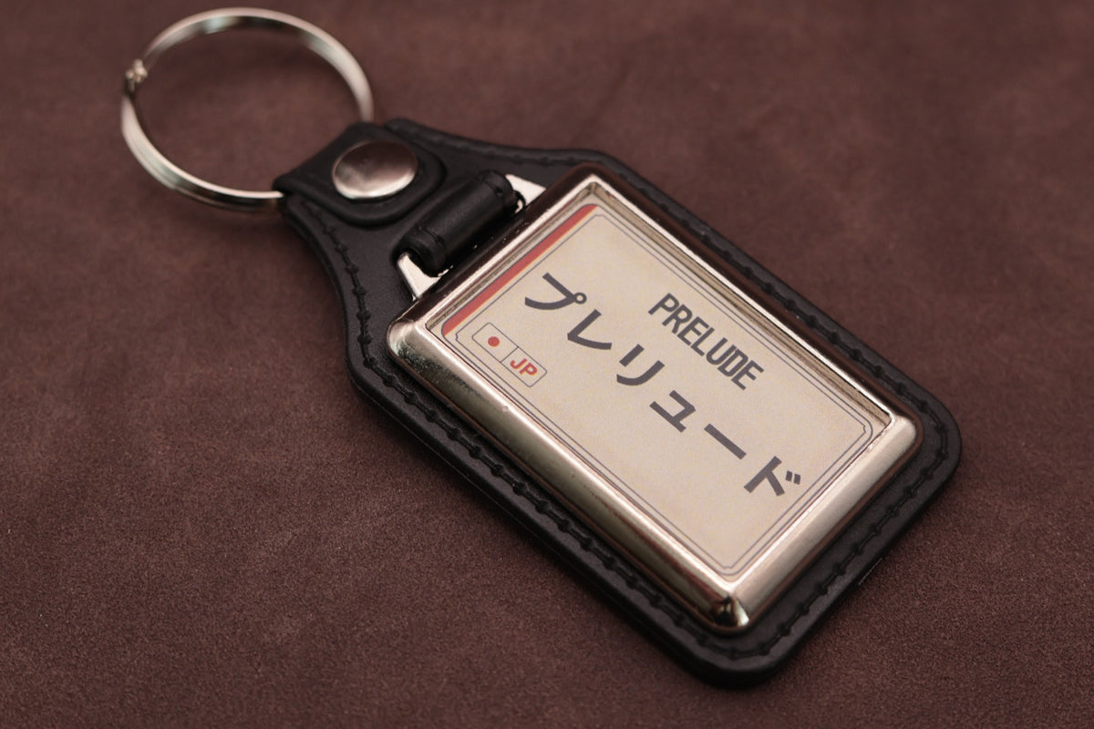 Honda Prelude Katakana keyring angled with the split ring at upper left, showing the printed insert and chromed frame