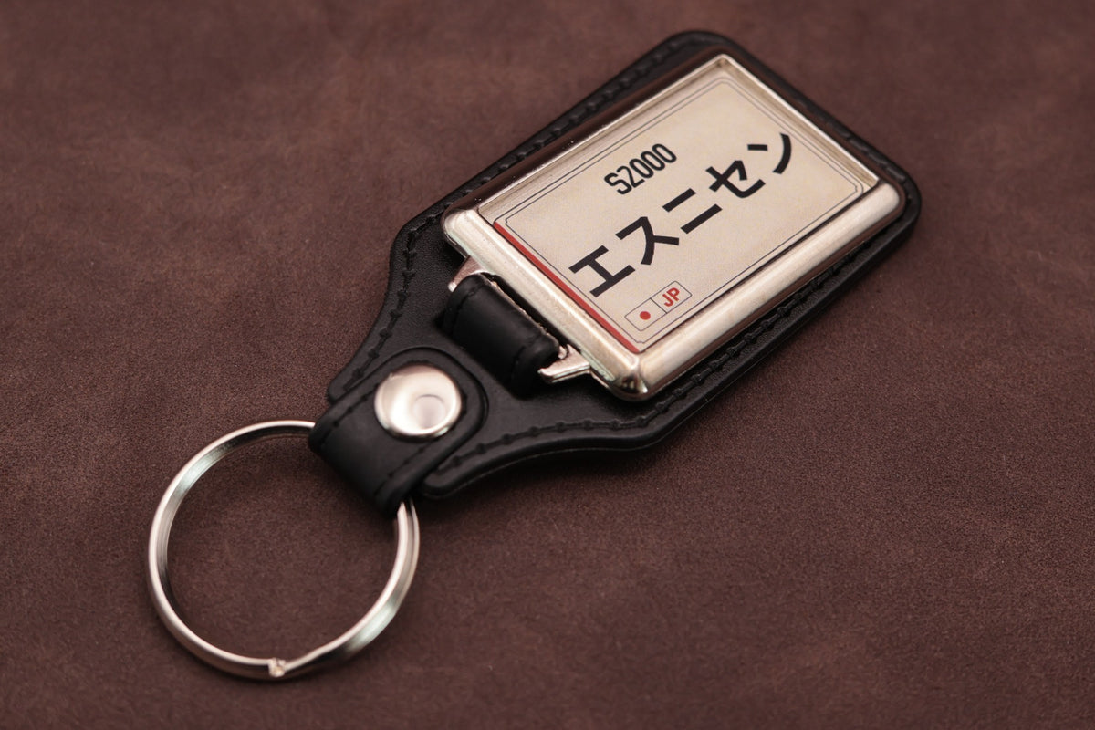 Honda S2000 Katakana keyring angled with the split ring at lower left, showing the cream insert and black leatherette fob