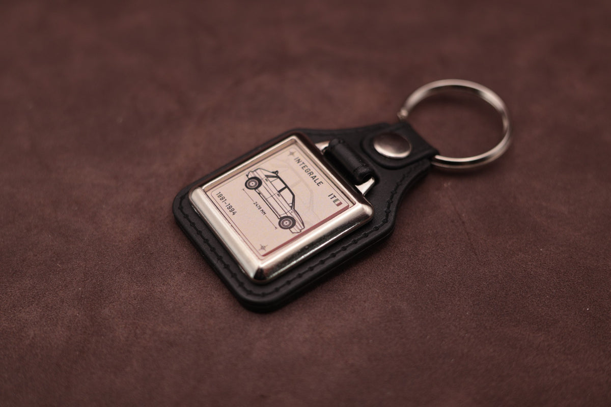 Lancia Delta Integrale Register Series keyring angled with the split ring at upper right and ivory vehicle artwork visible