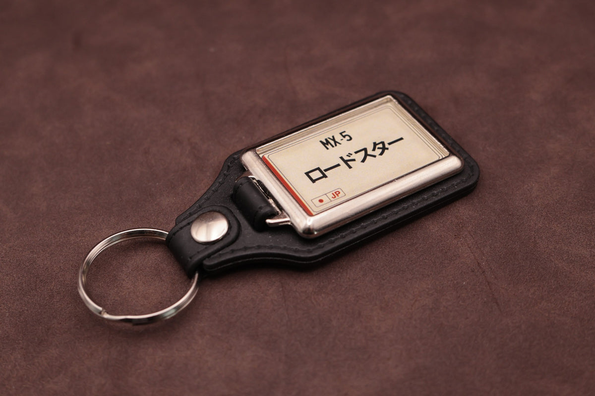 Mazda MX-5 Katakana keyring angled with the split ring at lower left, showing the cream insert and black leatherette fob