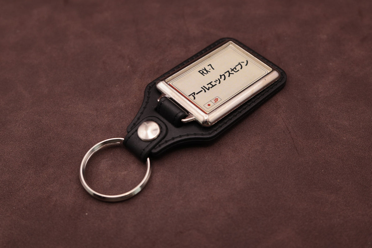 Mazda RX-7 Katakana keyring angled with the split ring at lower left, showing the cream insert and black leatherette fob