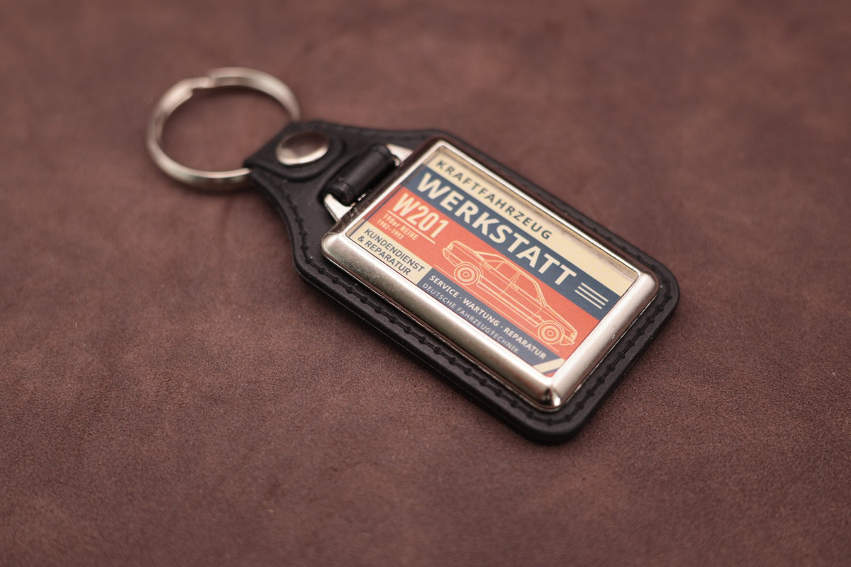 Mercedes-Benz W201 190 Werkstatt keyring angled with the split ring at lower left, showing the printed label and black leatherette fob