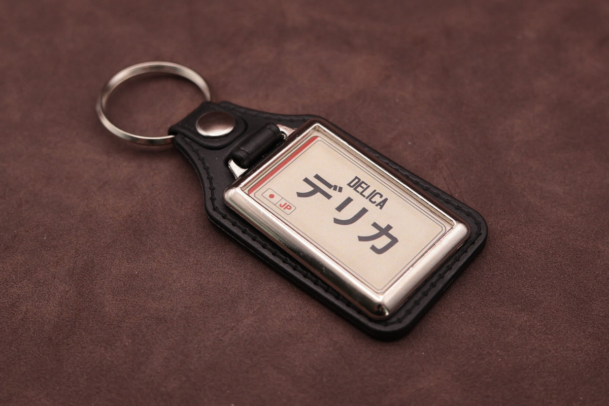 Mitsubishi Delica Katakana keyring angled with the split ring at upper left, showing the printed insert and chromed frame