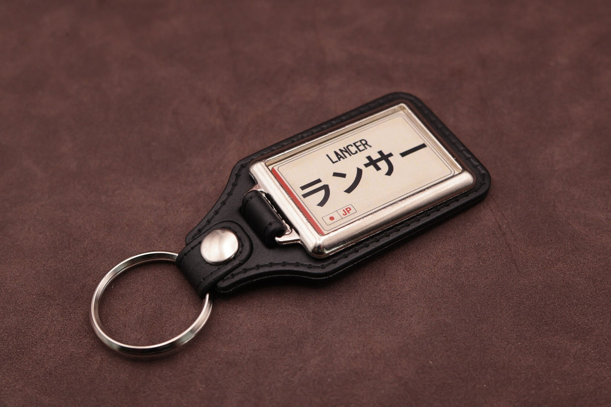 Mitsubishi Lancer Katakana keyring angled with the split ring at lower left, showing the cream insert and black leatherette fob