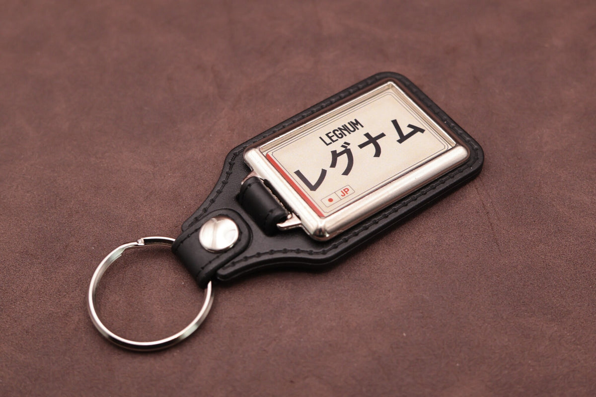 Mitsubishi Legnum Katakana keyring angled with the split ring at lower left, showing the cream insert and black leatherette fob