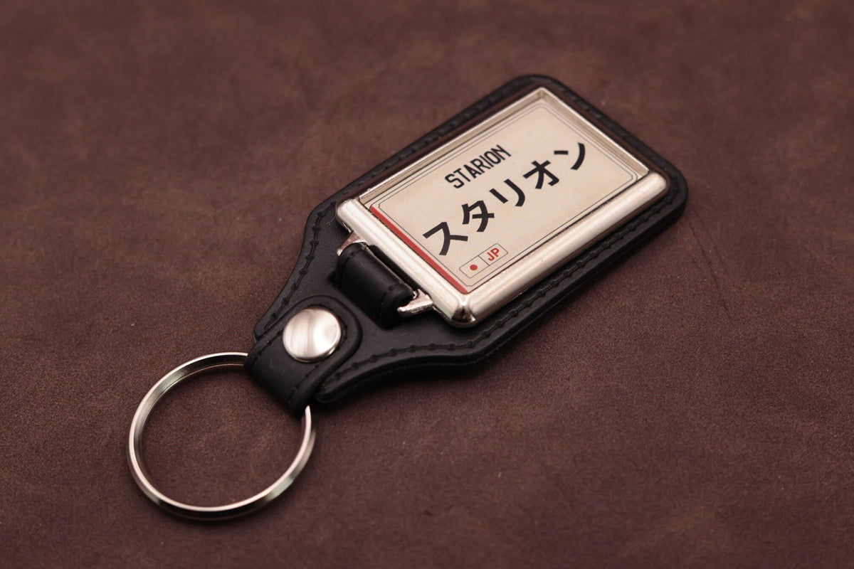Mitsubishi Starion Katakana keyring angled with the split ring at lower left, showing the cream insert and black leatherette fob