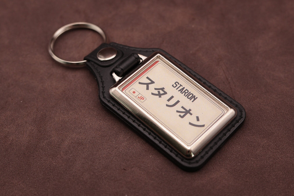 Mitsubishi Starion Katakana keyring angled with the split ring at upper left, showing the printed insert and chromed frame