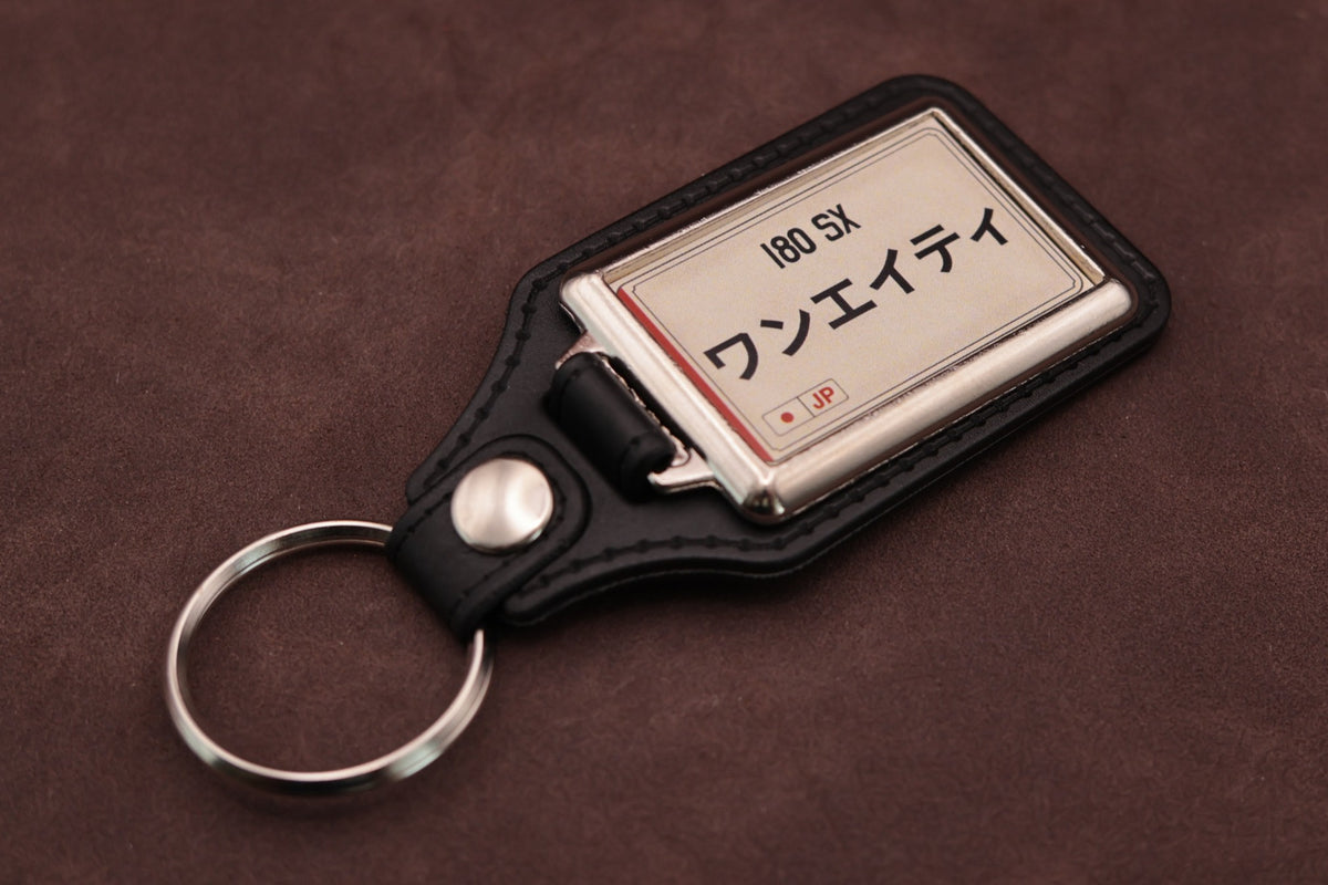Nissan 180SX Katakana keyring angled with the split ring at lower left, showing the cream insert and black leatherette fob
