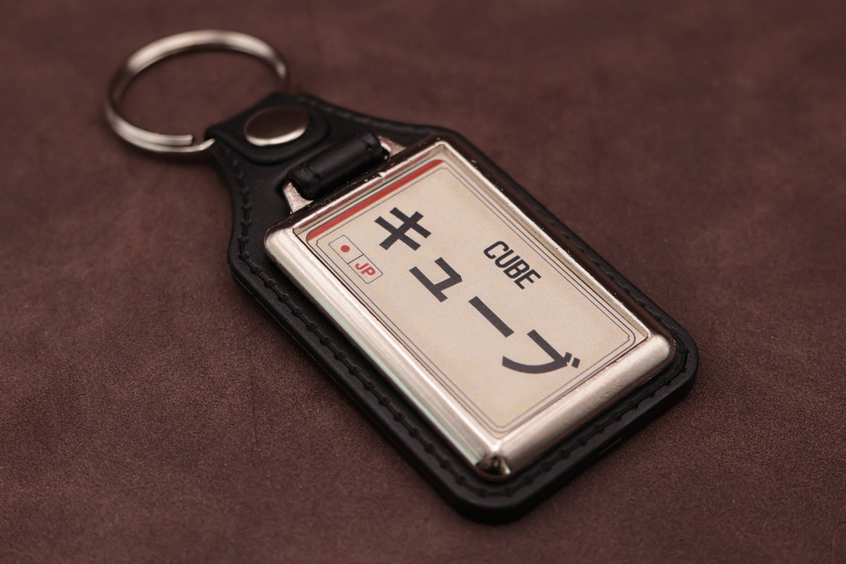 Nissan Cube Katakana keyring angled with the split ring at upper left, showing the printed insert and chromed frame