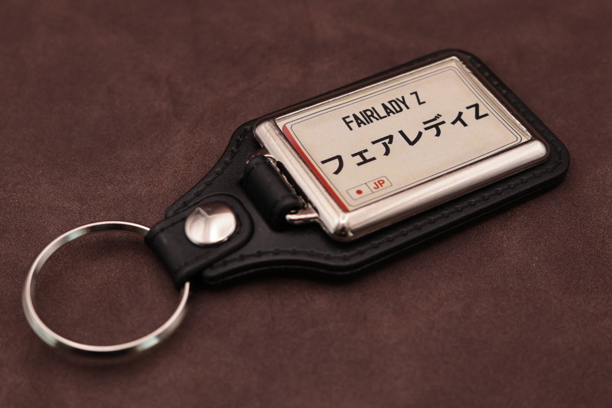 Nissan Fairlady Z Katakana keyring angled with the split ring at lower left, showing the cream insert and black leatherette fob