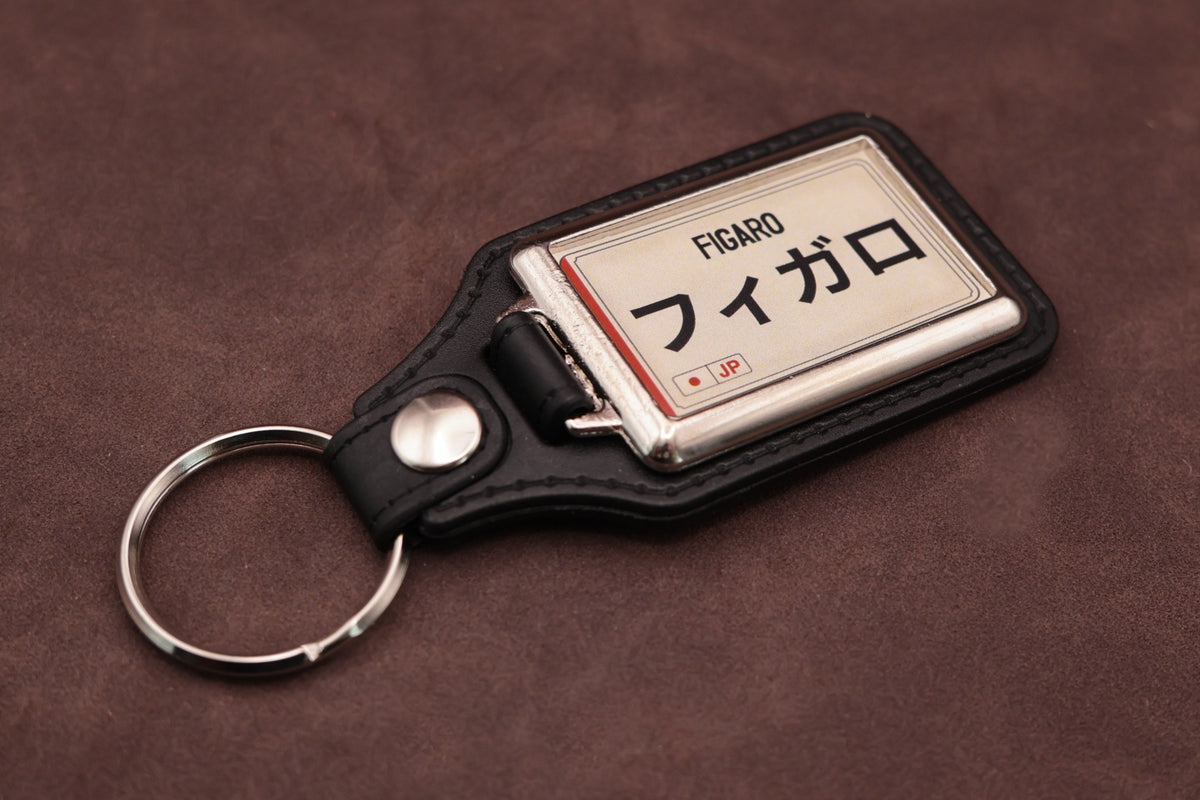 Nissan Figaro Katakana keyring angled with the split ring at lower left, showing the cream insert and black leatherette fob