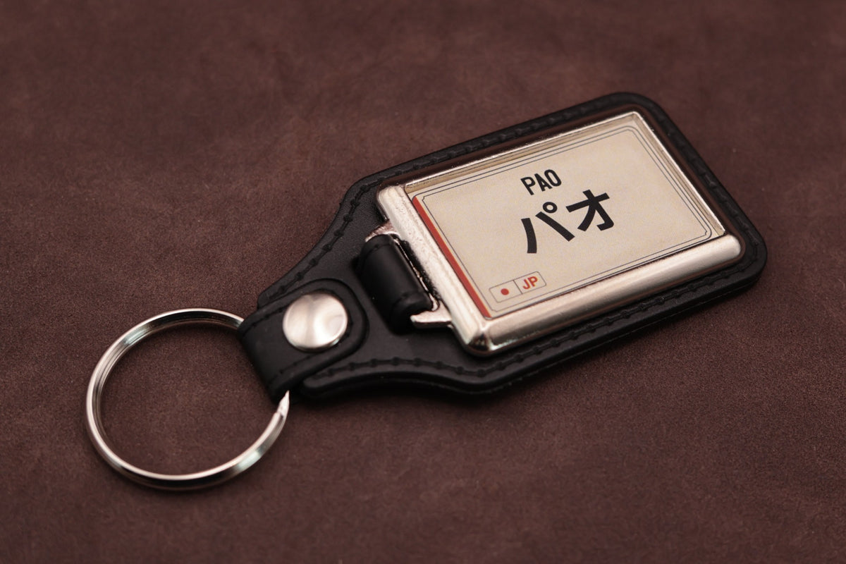 Nissan Pao Katakana keyring angled with the split ring at lower left, showing the cream insert and black leatherette fob