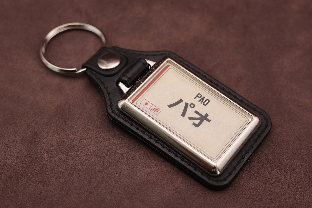 Nissan Pao Katakana keyring angled with the split ring at upper left, showing the printed insert and chromed frame