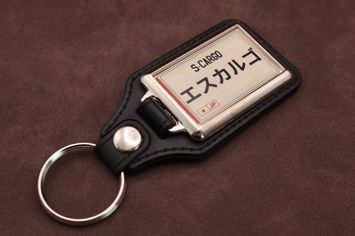 Nissan S-Cargo Katakana keyring angled with the split ring at lower left, showing the cream insert and black leatherette fob