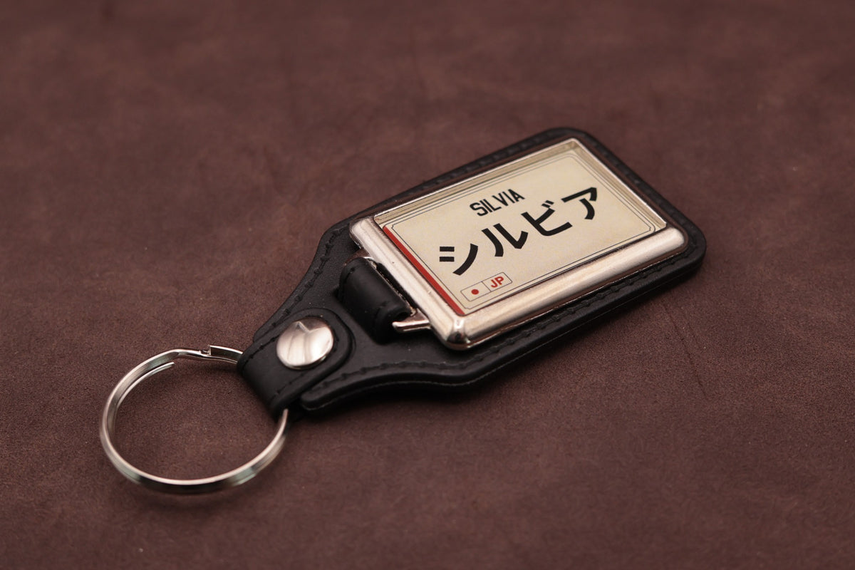 Nissan Silvia Katakana keyring angled with the split ring at lower left, showing the cream insert and black leatherette fob