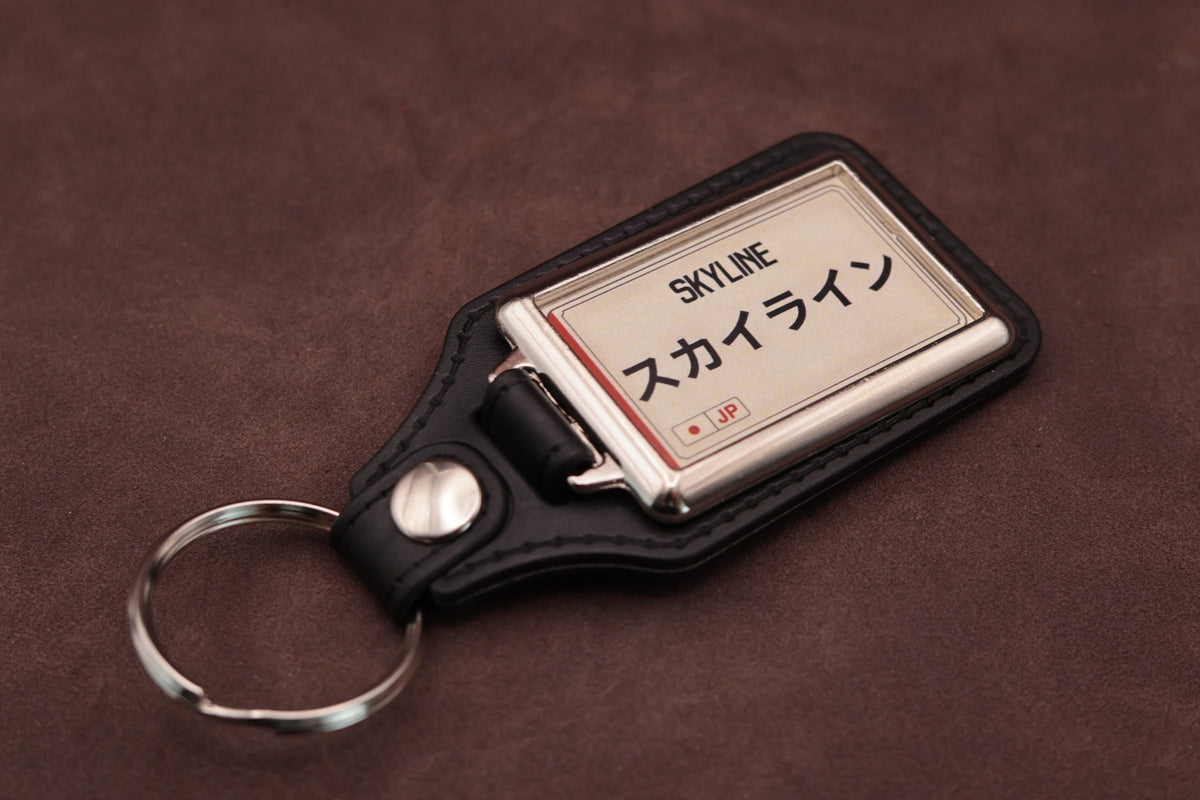 Nissan Skyline Katakana keyring angled with the split ring at lower left, showing the cream insert and black leatherette fob