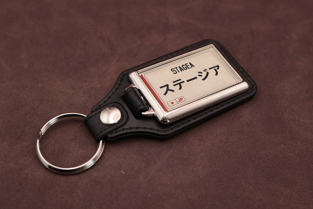 Nissan Stagea Katakana keyring angled with the split ring at lower left, showing the cream insert and black leatherette fob