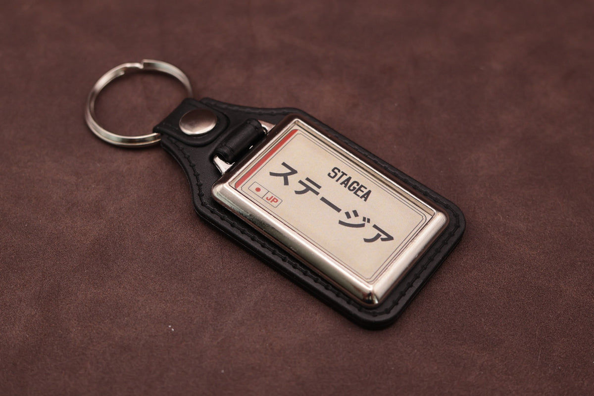 Nissan Stagea Katakana keyring angled with the split ring at upper left, showing the printed insert and chromed frame