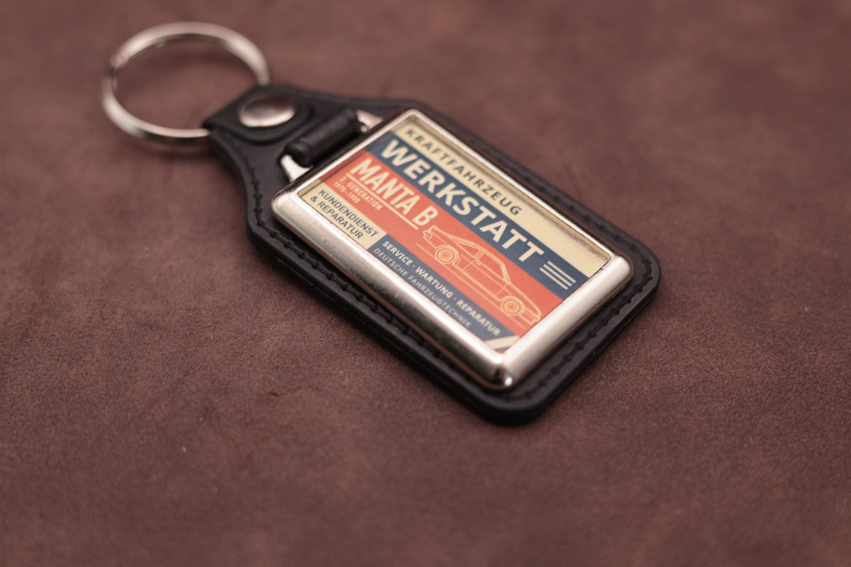 Opel Manta B Werkstatt keyring angled with the split ring at lower left, showing the printed label and black leatherette fob