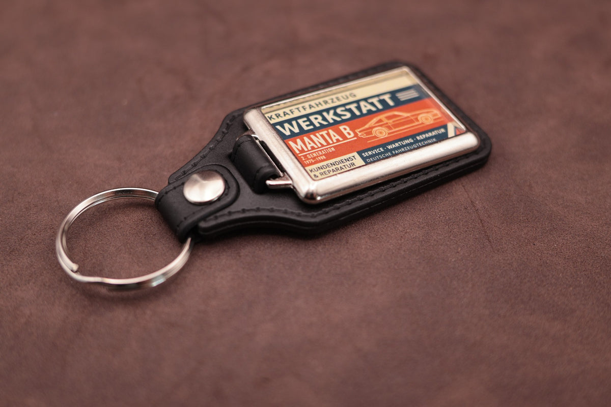 Opel Manta B Werkstatt keyring angled with the split ring at upper left, showing the printed label and chromed frame