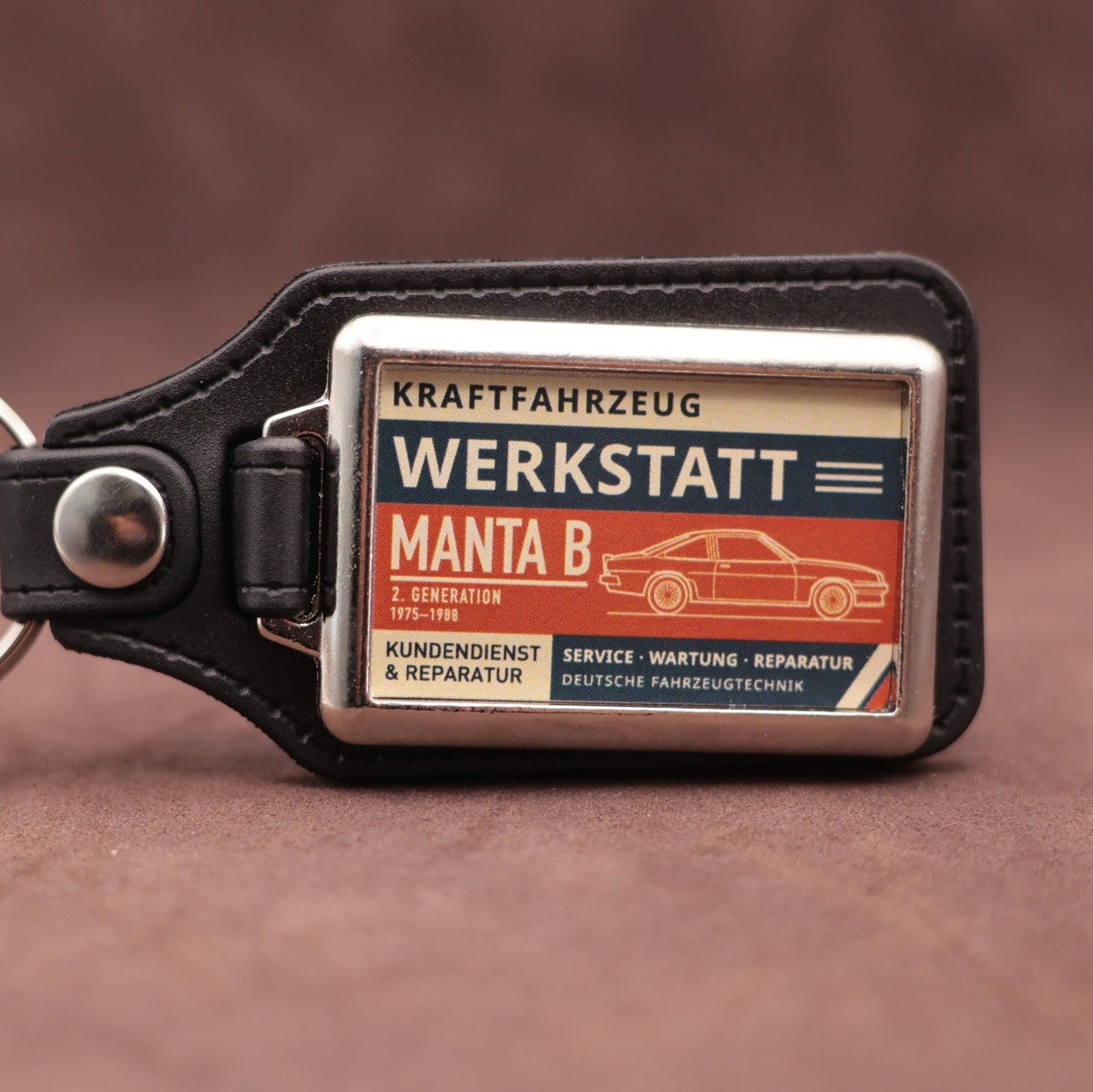 Opel Manta B Werkstatt keyring with cream, dark blue and rust red workshop lettering and vehicle illustration
