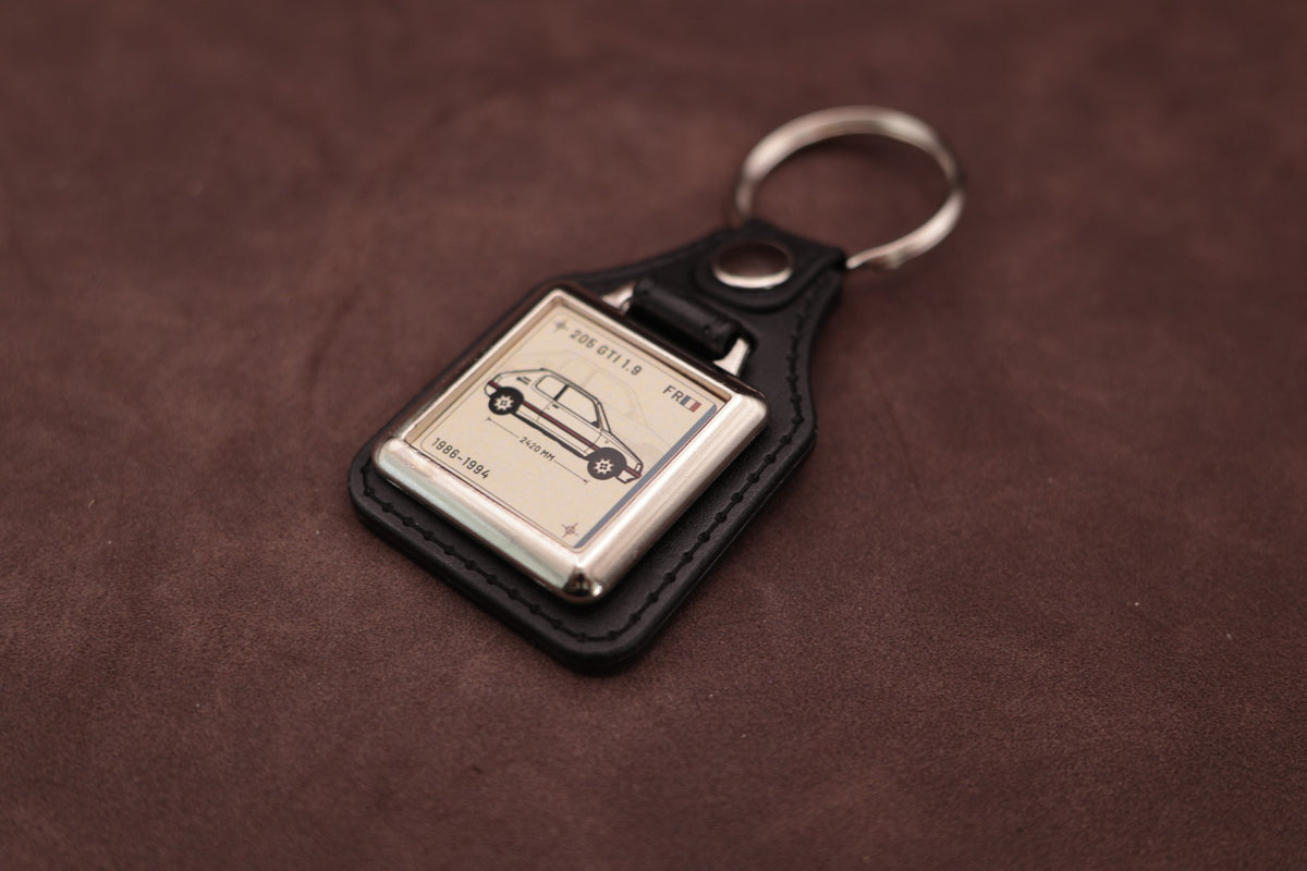 Peugeot 205 GTI 1.9 Register Series keyring angled with the split ring at upper right and ivory vehicle artwork visible