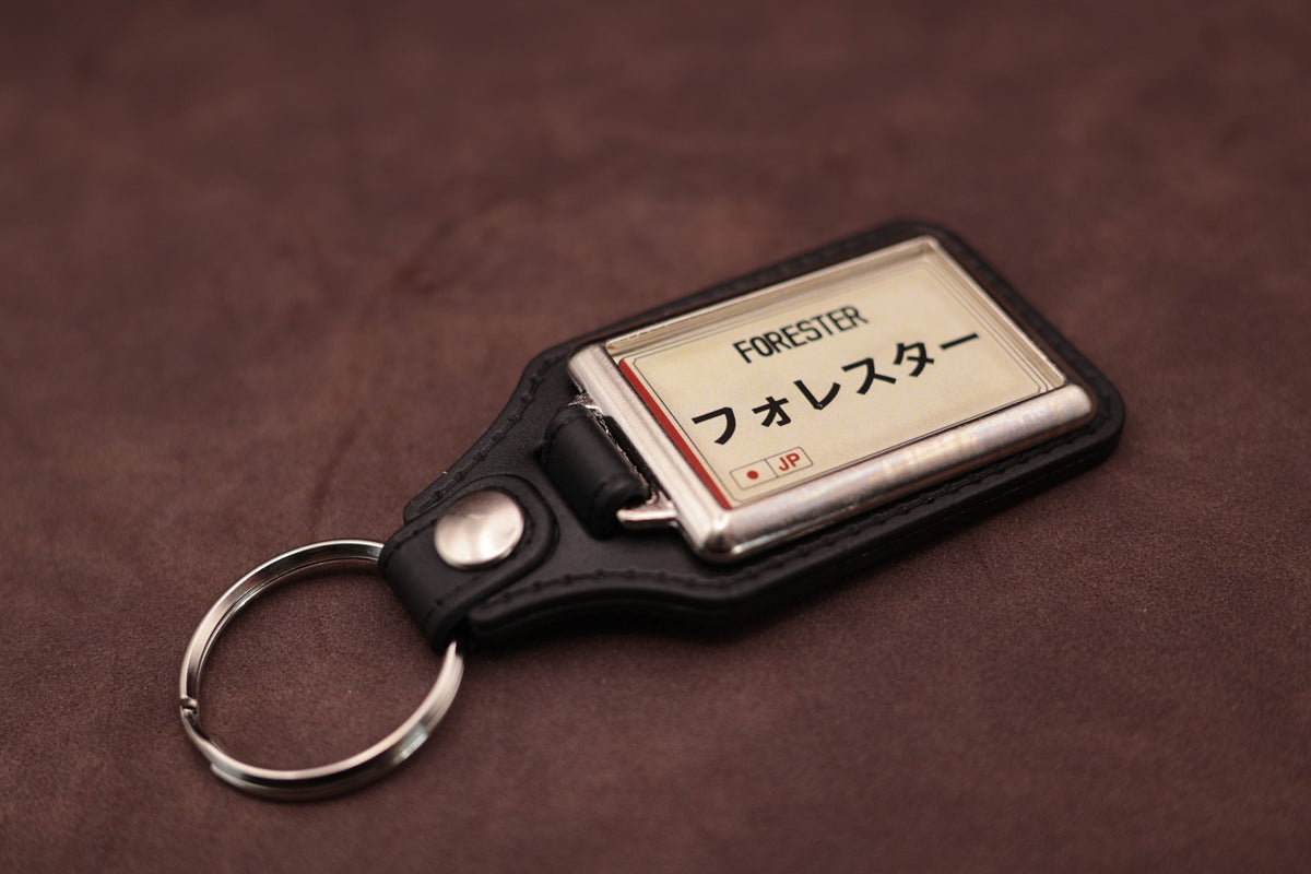 Subaru Forester Katakana keyring angled with the split ring at lower left, showing the cream insert and black leatherette fob
