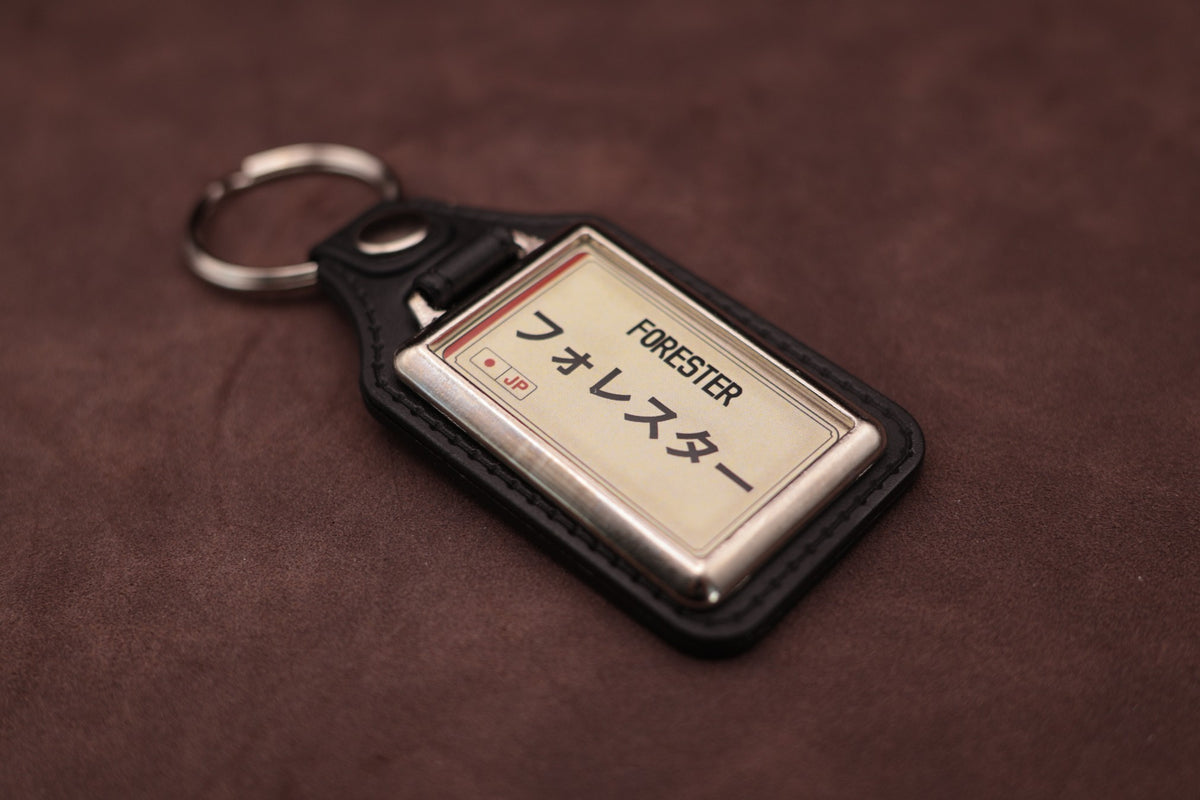 Subaru Forester Katakana keyring angled with the split ring at upper left, showing the printed insert and chromed frame