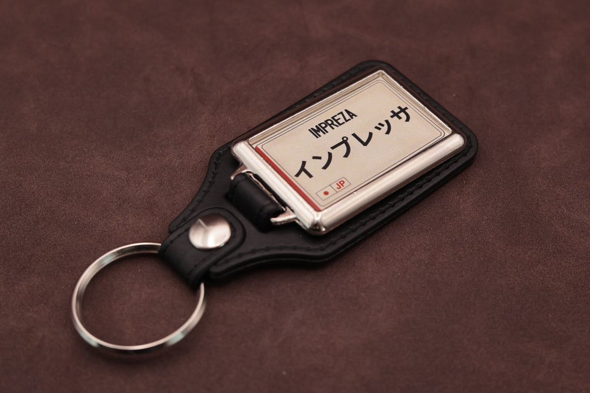 Subaru Impreza Katakana keyring angled with the split ring at lower left, showing the cream insert and black leatherette fob