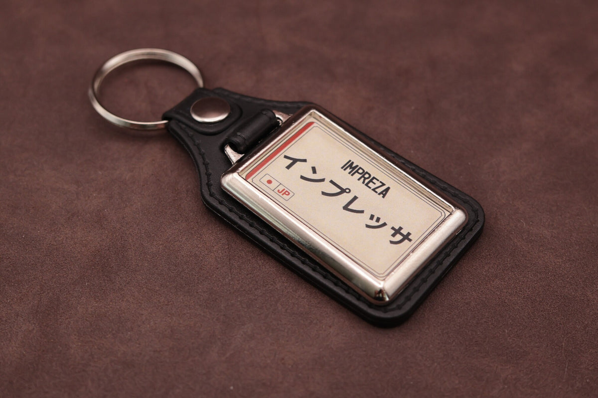 Subaru Impreza Katakana keyring angled with the split ring at upper left, showing the printed insert and chromed frame