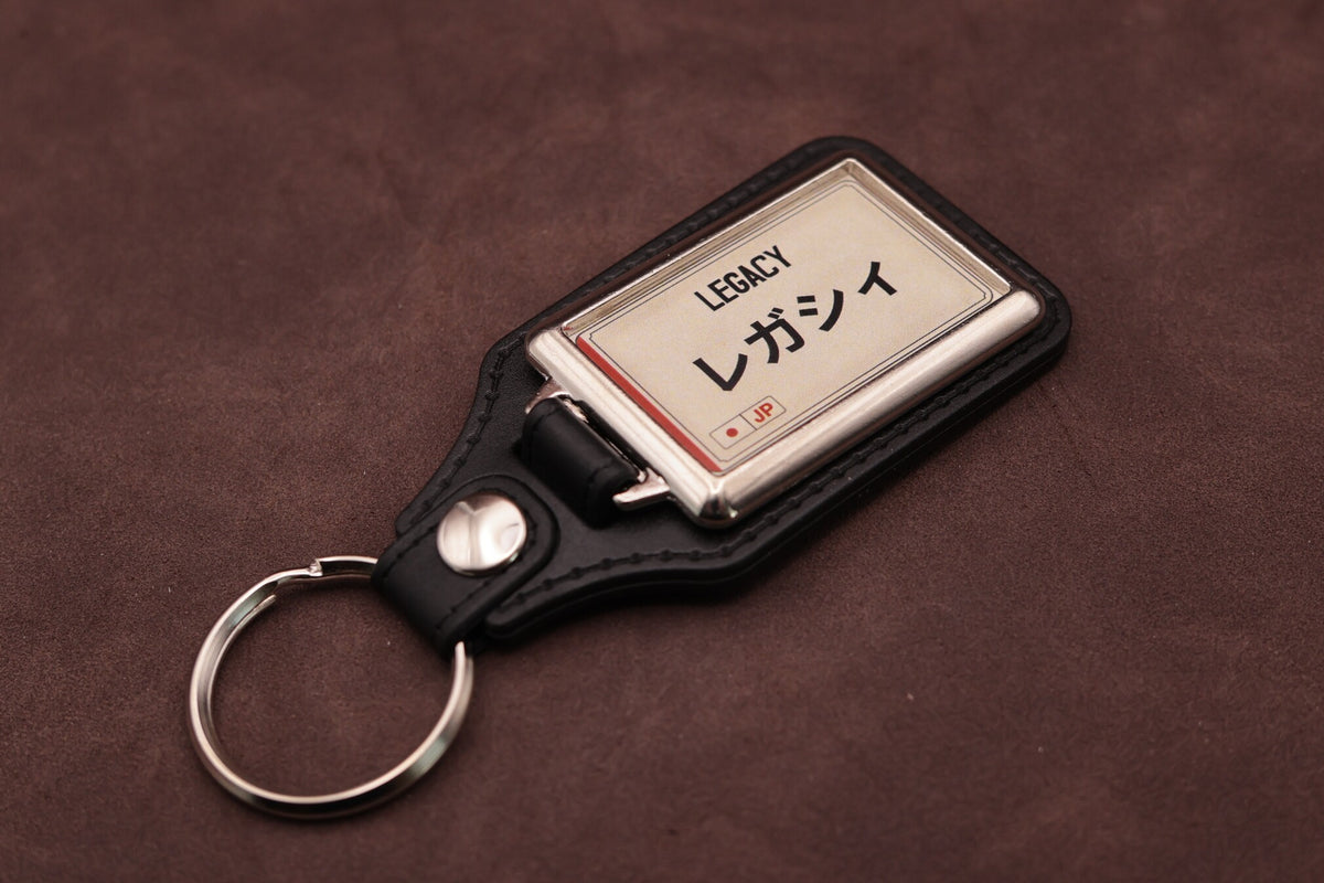 Subaru Legacy Katakana keyring angled with the split ring at lower left, showing the cream insert and black leatherette fob