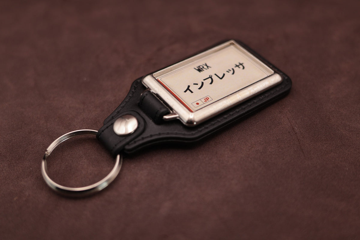 Subaru WRX Katakana keyring angled with the split ring at lower left, showing the cream insert and black leatherette fob