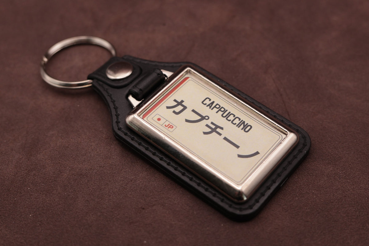Suzuki Cappuccino Katakana keyring angled with the split ring at upper left, showing the printed insert and chromed frame