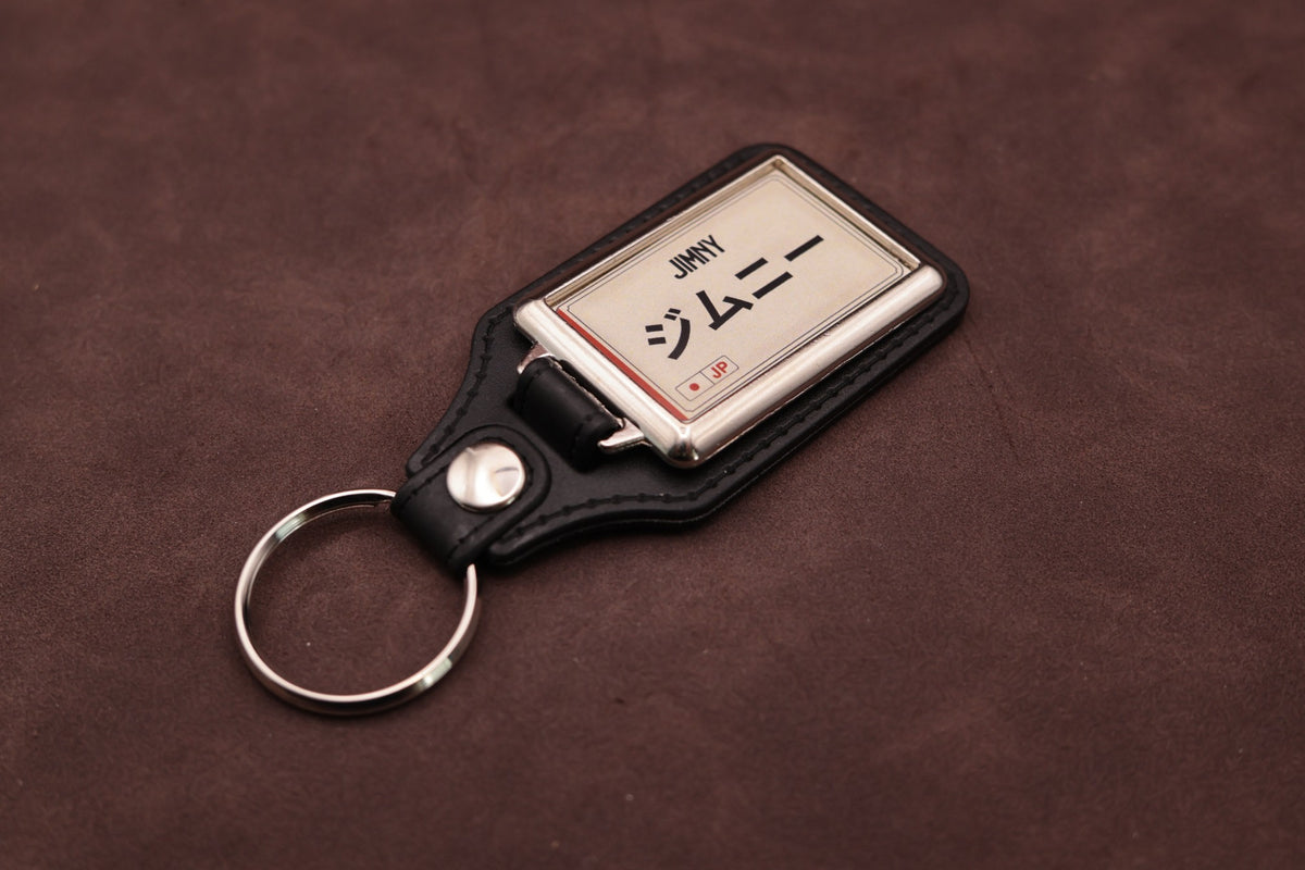 Suzuki Jimny Katakana keyring angled with the split ring at lower left, showing the cream insert and black leatherette fob