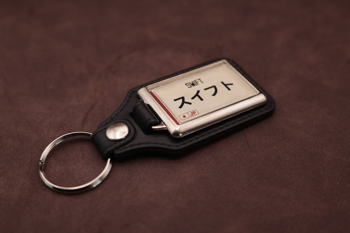 Suzuki Swift Katakana keyring angled with the split ring at lower left, showing the cream insert and black leatherette fob