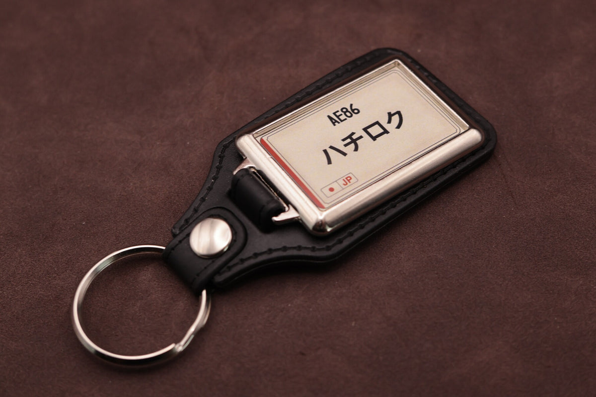 Toyota AE86 Katakana keyring angled with the split ring at lower left, showing the cream insert and black leatherette fob