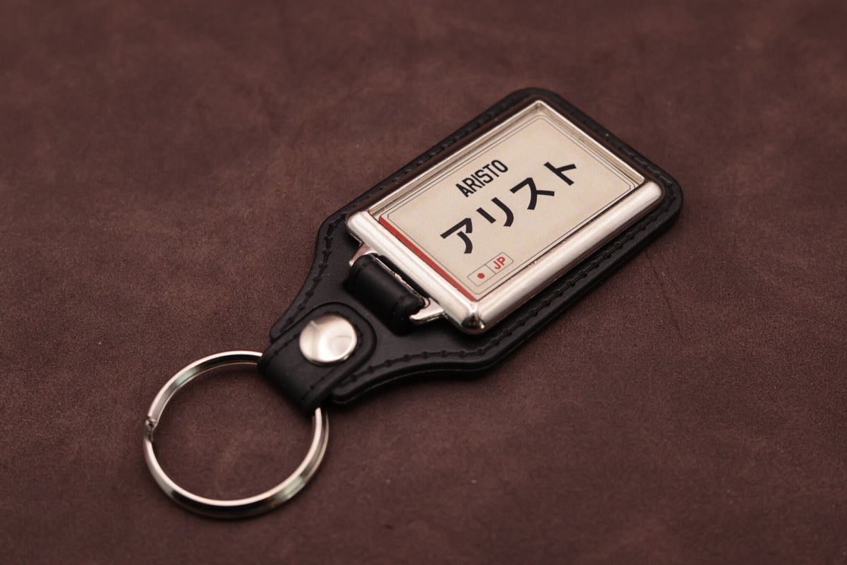 Toyota Aristo Katakana keyring angled with the split ring at lower left, showing the cream insert and black leatherette fob