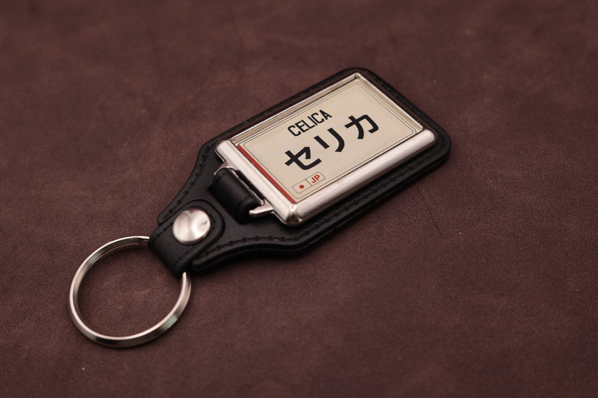 Toyota Celica Katakana keyring angled with the split ring at lower left, showing the cream insert and black leatherette fob