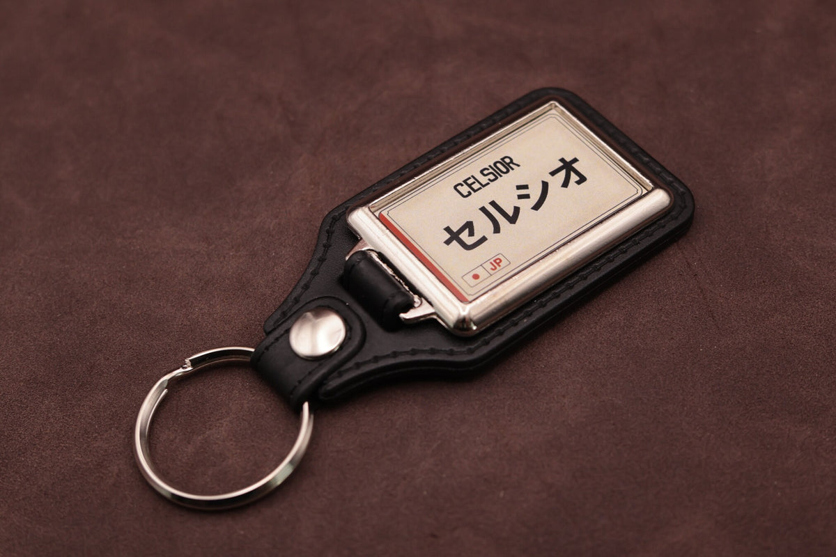 Toyota Celsior Katakana keyring angled with the split ring at lower left, showing the cream insert and black leatherette fob