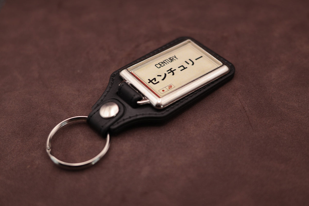 Toyota Century Katakana keyring angled with the split ring at lower left, showing the cream insert and black leatherette fob