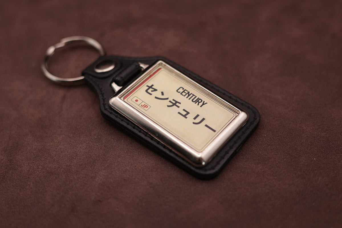 Toyota Century Katakana keyring angled with the split ring at upper left, showing the printed insert and chromed frame