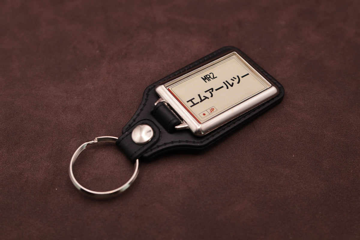 Toyota MR2 Katakana keyring angled with the split ring at lower left, showing the cream insert and black leatherette fob