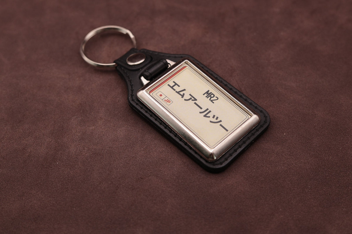 Toyota MR2 Katakana keyring angled with the split ring at upper left, showing the printed insert and chromed frame
